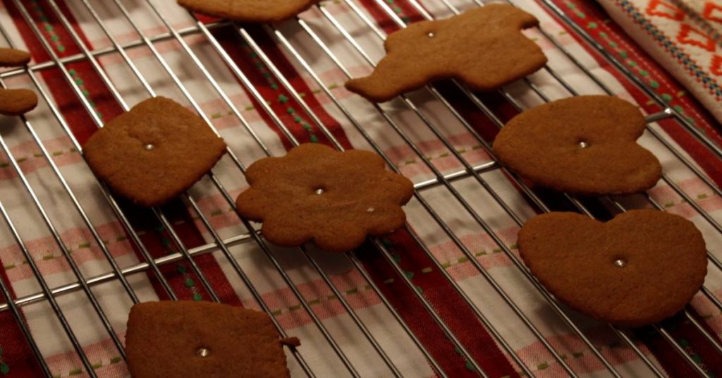Old fashioned gingerbread cut out cookies decorated with small silver candy balls cooling on rack on tea towel