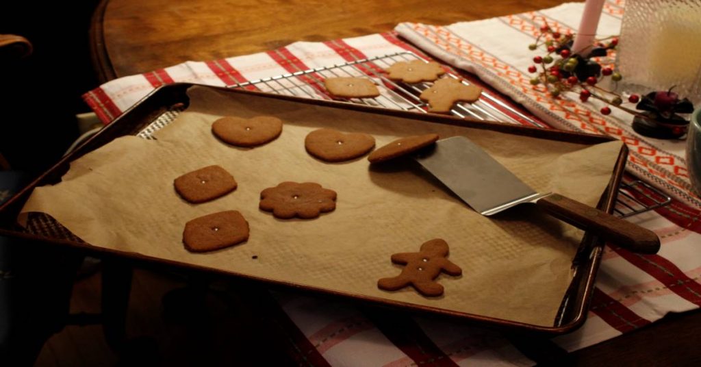 old fashioned gingerbread cut out cookies baked on cookie sheet with spatula under one to show it being removed to cooling rack on decorated diningroom table