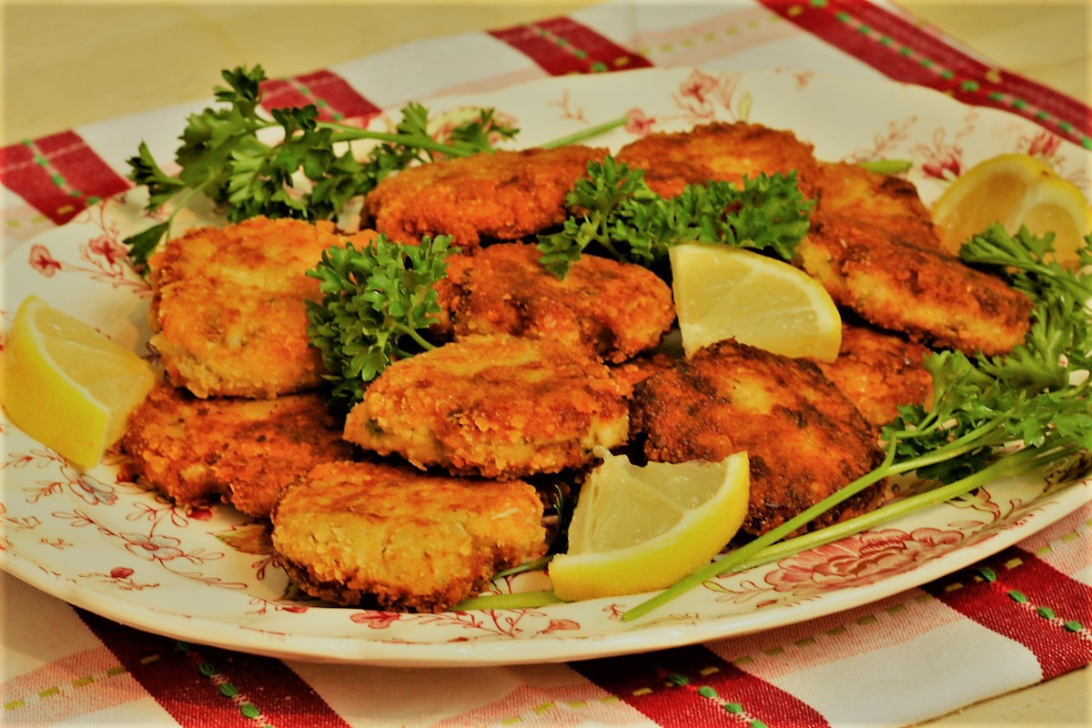 A plate full of deviled crab cakes with lemon wedges and parsley