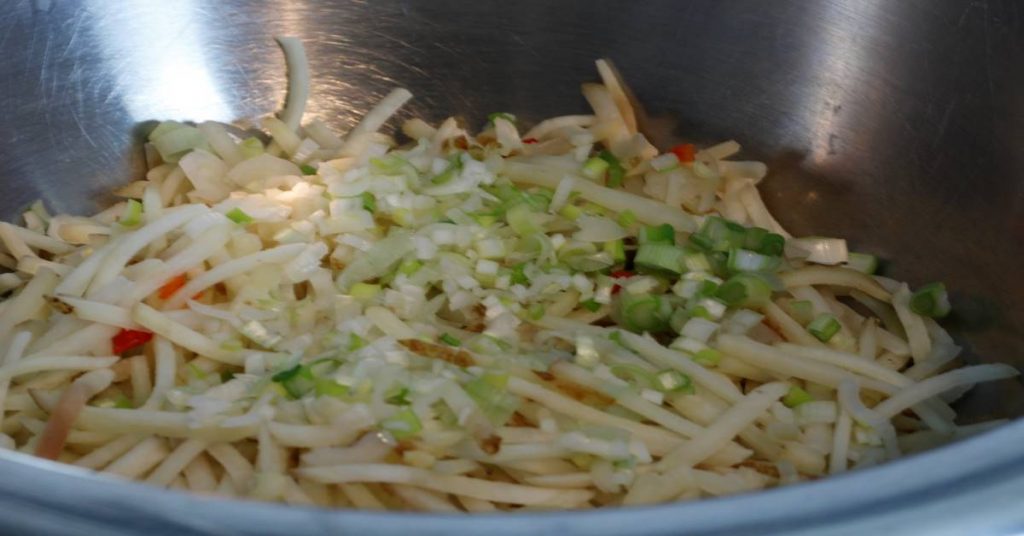 Bowl of O'Brien hashbrowns and chopped green onions for cheesy potatoes recipe.